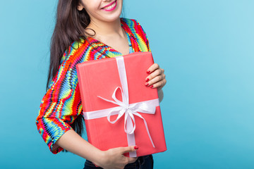 Wall Mural - Close up of cheerful good looking young brunette woman holding a red gift box in her hands, but against a blue background. Concept holidays and presents