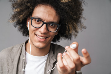 Photo closeup of young happy man with afro hairstyle smiling and giving earphone at camera