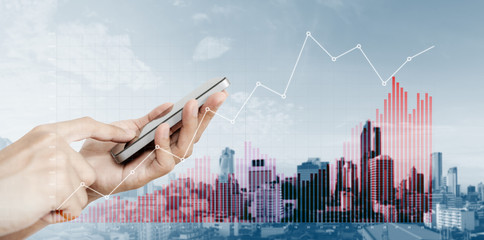 Hand holding mobile smart phone with raising financial graphs, on city background