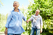 © Seventyfour - Portrait of happy senior woman leading husband by hand while enjoying walk in Summer park