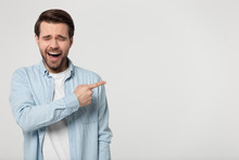 Giggling Guy Pointing Finger At Copyspace Isolated On Grey Background