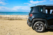 Black summer car on the sunny sandy beach. Blue clear sunshine sky view in distance. 
