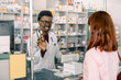 © sofiko14 - medicine, pharmaceutics, health care and people concept - happy young African man pharmacist giving drug to young pretty woman customer at drugstore