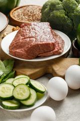 Wall Mural - close up view of raw meat on wooden chopping board near eggs and cucumbers, , ketogenic diet menu