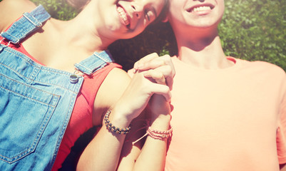 love and people concept - close up of happy teenage couple lying on grass and holding hands with wristbands at summer