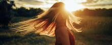 Young Blond Woman Stands On Meadow With Loose Hair Lit By Sun.