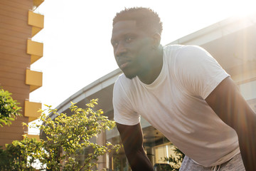 Wall Mural - Portrait of African American man taking a rest during jogging. Young male fit person doing exercise and taking a break in city park