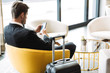 Photo of caucasian young man sitting in hotel hall with smartphone and suitcase during business trip