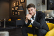 © Drobot Dean - Portrait of beautiful young businessman wearing formal black suit sitting on armchair in hotel hall