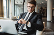 © Drobot Dean - Portrait of young businesslike man using laptop computer and looking at his wristwatch in hotel hall