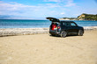 Black summer car on the sunny sandy beach. Blue clear sunshine sky view in distance. 