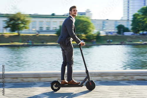 Fotomural Young business man in a suit riding an electric scooter on a business meeting