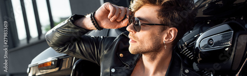 panoramic shot of young man sitting near motorcycle and holding sunglasses while Poster Mural XXL