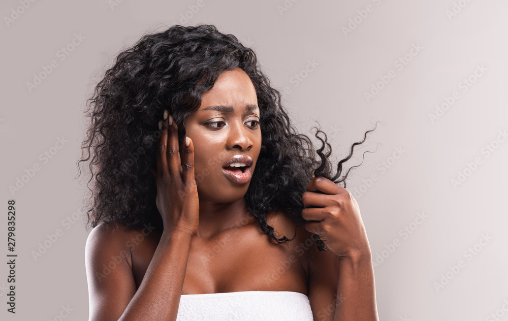 Sad african woman looking at dry edges of damaged hair - obrazy, fototapety, plakaty 