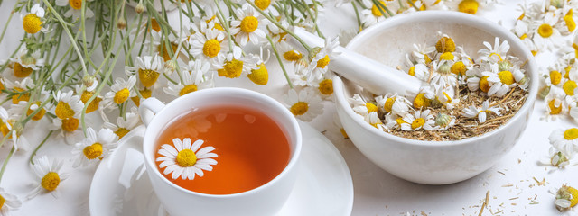 Rural still-life - cup of brewed chamomile tea on the background of a bouquet of daisies, closeup