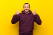 © luismolinero - Colombian man with sweatshirt over yellow wall with thumbs up gesture and smiling