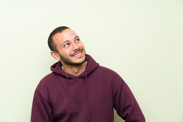 Wall Mural - Colombian man with sweatshirt over green wall laughing and looking up