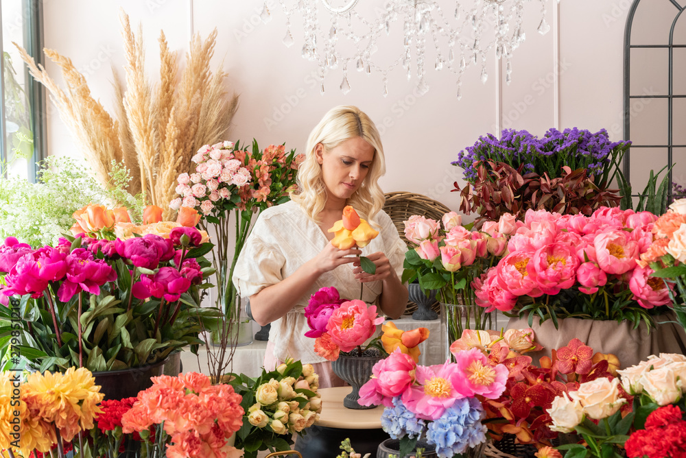 Beautiful blonde florist woman picks up flowers and creates wonderful bouquet - obrazy, fototapety, plakaty 