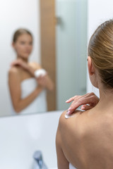 Wall Mural - Woman applying body cream on shoulder in bathroom