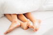 © Yingyaipumi - Close up of four feet of couple in white bed. Men and women's legs under a white blanket on a white bed. Lovely love scene concept.