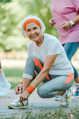 Wall Mural - selective focus of happy senior woman sitting and tying shoelaces in park