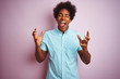 © Krakenimages.com - Young american man with afro hair wearing blue shirt standing over isolated pink background celebrating mad and crazy for success with arms raised and closed eyes screaming excited. Winner concept