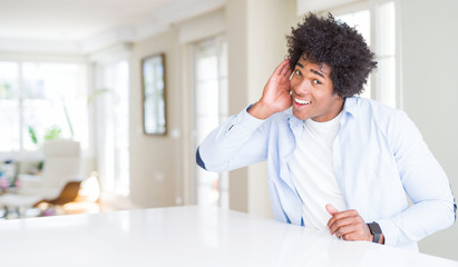 Canvas Print - African American man at home smiling with hand over ear listening an hearing to rumor or gossip. Deafness concept.