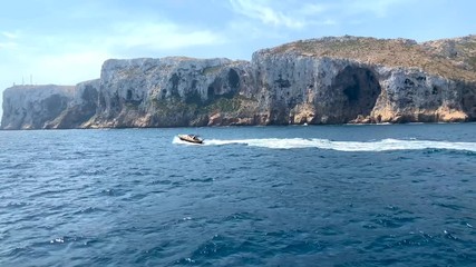 Wall Mural - A boat sailing in the Mediterranean sea, near the Denia and Javea coast in Spain. The cliff of San Antonio Cape is in the background.