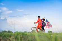 Independence Day Concept - Two Happy Young Local Boy Riding Old Bicycle At Paddy Field Holding A Malaysian Flag