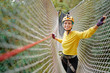 © Loginova - Young woman with climbing gear in an adventure extreme park climbing or passing on the rope road.