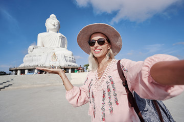 Traveling by Thailand. Pretty young woman in hat taking selfie in the Big Buddha Temple, famous Phuket sightseeing.