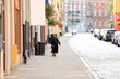 Stara kobieta w czarnym stroju, pochylona idzie chodnikiem przez miasto.