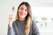 © Krakenimages.com - Young beautiful woman holding silver spoon at home with a happy face standing and smiling with a confident smile showing teeth