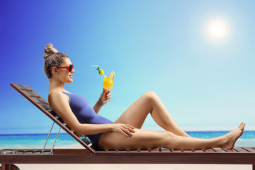 Wall Mural - Young woman sunbathing on a beach with a cocktail