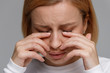 Close up of young woman has a problem with contact lenses, rubbing her swollen eyes due to pollen, dust allergy. Dry eye syndrome, watery, itching. Isolated on grey background