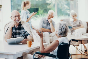 Wall Mural - Smiling senior man with book talking with elderly woman in the nursing house