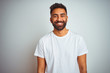 Young indian man wearing t-shirt standing over isolated white background with a happy and cool smile on face. Lucky person.
