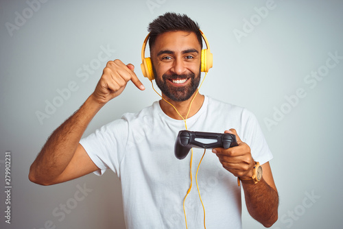 Arab indian gamer man playing video game using headphones over isolated white ba Wallpaper Mural