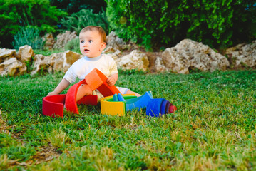 Wall Mural - Baby girl playing with a waldorf material, a rainbow of wood montessori, in nature.