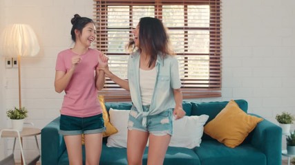 Wall Mural - Asian Lesbian lgbtq women couple dancing at home, Young Asia lover female feeling happy fun dance, singing, listening music while in living room at home concept. Slow motion.