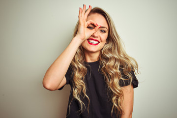 Wall Mural - Young beautiful woman wearing black t-shirt standing over white isolated background doing ok gesture with hand smiling, eye looking through fingers with happy face.