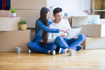 Sticker - Young asian couple sitting on the floor of new house arround cardboard boxes using laptop and drinking a cup of coffee