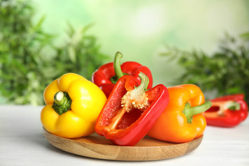 Wooden cutting board with ripe bell peppers on table against blurred background