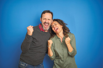 Poster - Beautiful middle age couple together standing over isolated blue background very happy and excited doing winner gesture with arms raised, smiling and screaming for success. Celebration concept.