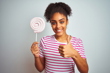 African american teenager woman eating colorful candy over isolated white background happy with big smile doing ok sign, thumb up with fingers, excellent sign