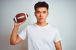 © Krakenimages.com - Young asian chinese sportsman holding rugby ball standing over isolated white background with a confident expression on smart face thinking serious