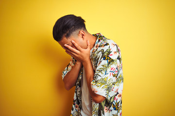 Young brazilian man on vacation wearing summer floral shirt over isolated yellow background with sad expression covering face with hands while crying. Depression concept.