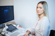 © olgasparrow - Blonde female doctor near an ultrasound monitor is looking at the camera.