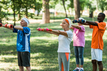 Wall Mural - selective focus of pensioners in sportswear training with dumbbells in park