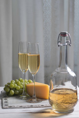 two glasses of white wine with cheese and green grapes on a grey background